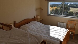 A bedroom with two beds, a window with a view of a forest, and a radiator.