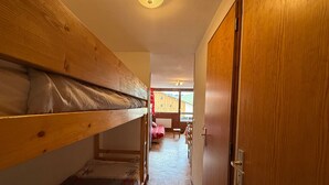 Un pasillo estrecho con literas a un lado y una puerta de madera al otro.