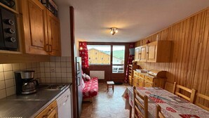 Cocina compacta con armarios de madera, cafetera y ventana con vistas a edificios.