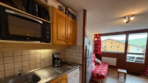 Una cocina compacta con microondas, cafetera y lavavajillas. Hay un pequeño comedor con una mesa y un banco.