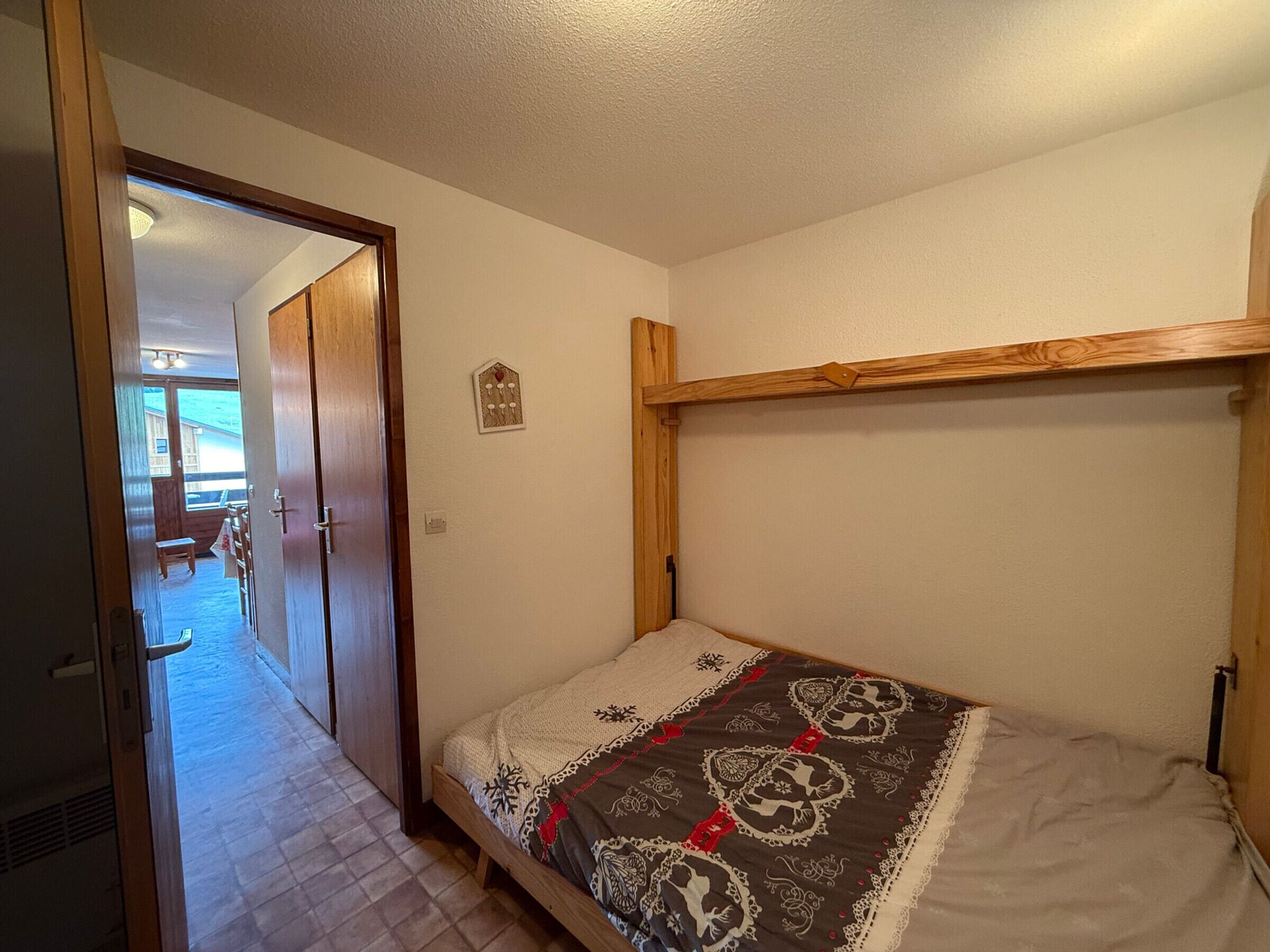 Een kleine eenpersoonskamer met een houten hoofdbord, een klein decoratief object aan de muur en een deur naar een balkon.