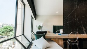 Et moderne hotelværelse med et stort vindue, en seng med hvide sengetøj, et skrivebord med en bærbar computer, en stol og en potteplante.