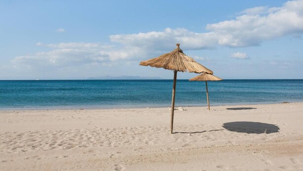 Ein Strand mit zwei Reetsonnenhütten und freiem Blick auf den Ozean.
