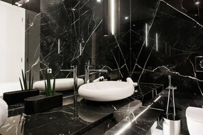 Une salle de bain moderne avec des comptoirs en marbre noir, une baignoire blanche et un lavabo rond blanc.
