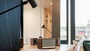 A modern room with a wooden desk, a book titled 'ATHENS RIVIERA', a Marshall speaker, and a view of a cityscape through large windows. - Executive Luxury Suite Athens Riviera by The Olon (Glyfada)