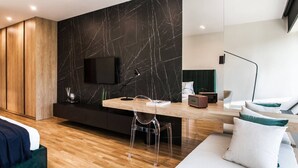 A modern living room with a wooden floor, a black marble wall, a flat-screen TV, a wooden coffee table, and a green sofa. - Executive Luxury Suite Athens Riviera by The Olon (Glyfada)