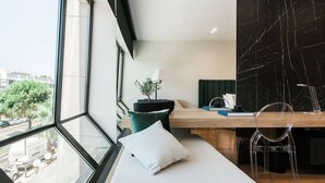 Quarto de hotel moderno com uma janela grande, uma cama, uma escrivaninha e uma cadeira.