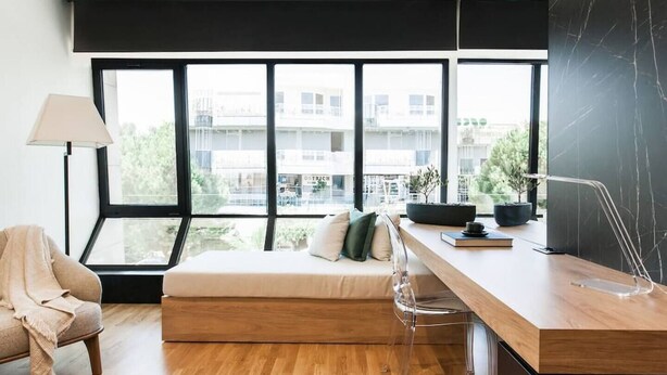 Um quarto moderno com uma janela grande, um sofá, uma escrivaninha e uma luminária.