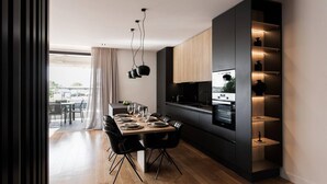 Una cucina moderna con zona pranzo, con un tavolo in legno apparecchiato per quattro persone, forno a incasso e lampada a sospensione nera.