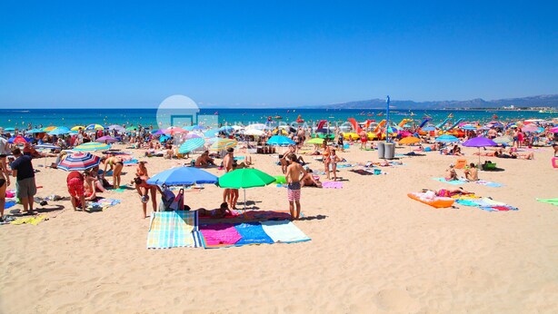 Una playa concurrida, con numerosos paraguas de colores y gente tomando el sol.