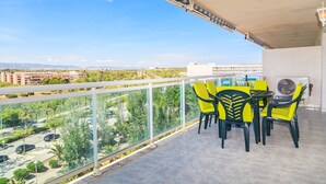 Un balcón con sillas amarillas y una mesa, con vistas a un paisaje urbano con edificios y zonas verdes.