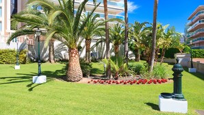 Un jardín bien cuidado con palmeras, flores rojas y una estatua.