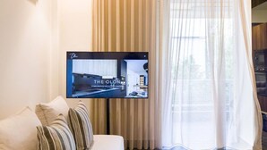 A modern living room with a flat-screen TV mounted on the wall, a sofa with striped cushions, and a large window with sheer curtains.