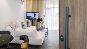 A modern hotel room with a sofa, a small round table, a TV, and a large window with curtains.