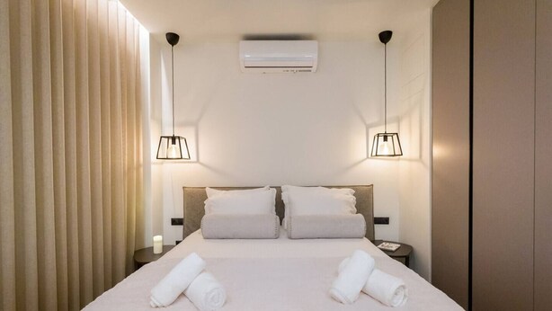 A hotel room with a large bed, two bedside lamps, an air conditioner, and a nightstand with a candle.