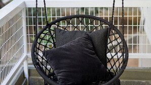 A black wicker swing chair with cushions on a porch.
