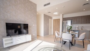 A modern living room with a flat-screen TV, a glass coffee table, and a dining area with chairs and a table. - Nasma Luxury Stays - Dubai Hills (Dubai)