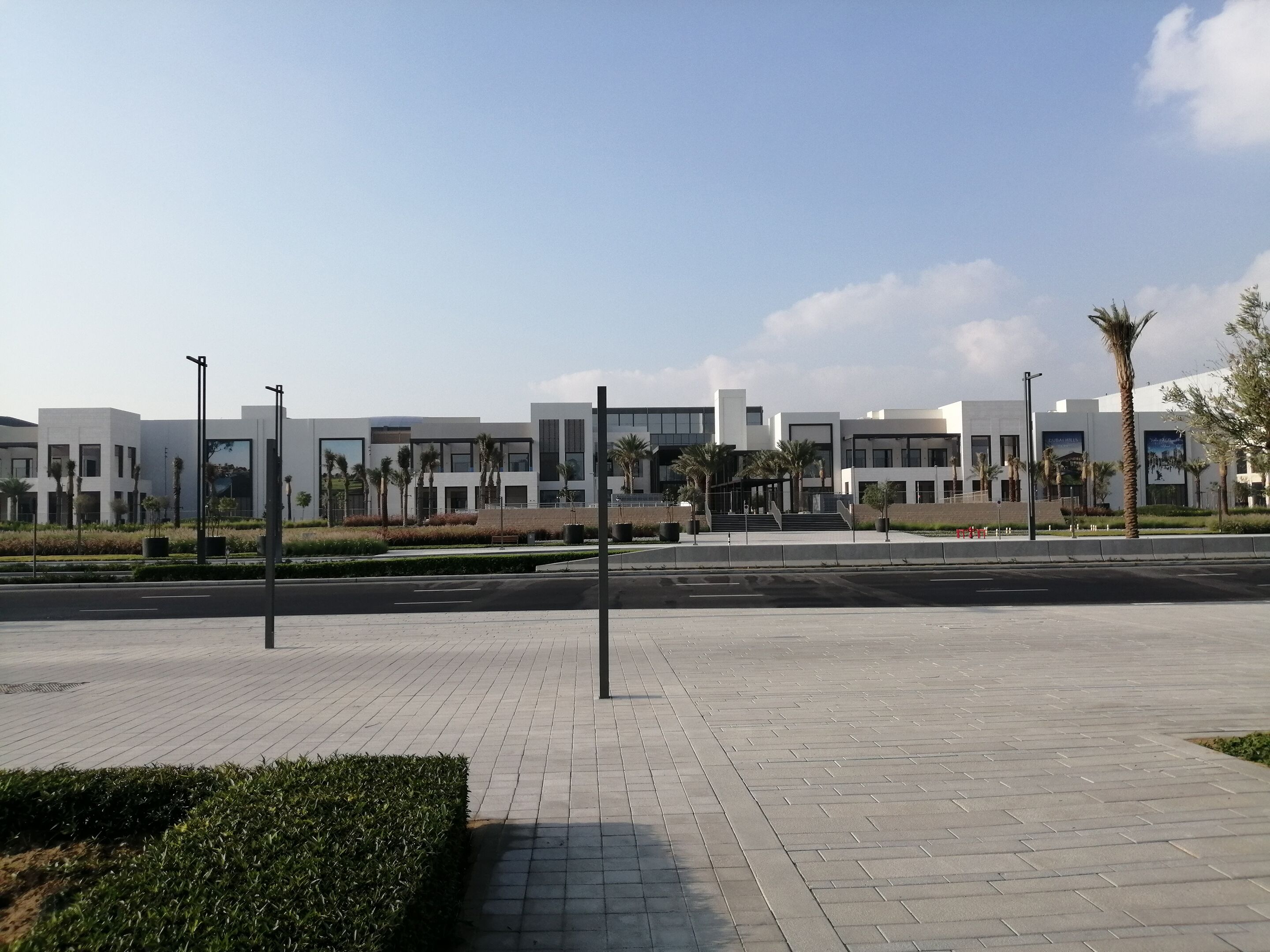Un ensemble immobilier moderne doté d’une allée pavée, de palmiers et offrant une vue sur un ciel dégagé.