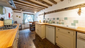A kitchen with wooden beams, a stove, a dishwasher, and a window with curtains. - Oak House (Rye)