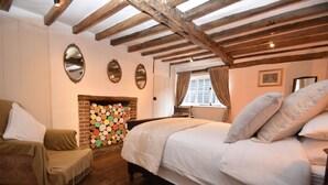 A bedroom with a large bed, a wooden ceiling, a fireplace, and a window with curtains. - Oak House (Rye)