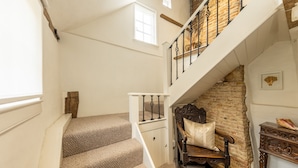 A staircase with carpeted steps leading to a second floor, a wooden bench, a small wooden cabinet, and a stone wall. - Oak House (Rye)