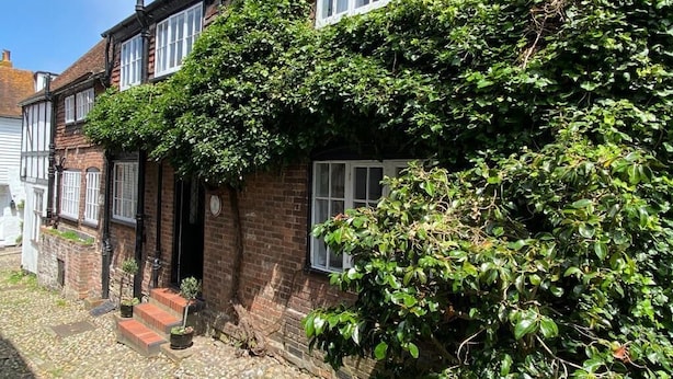 A traditional brick house with a steeply pitched roof, white window frames, and a brick chimney. - Oak House (Rye)
