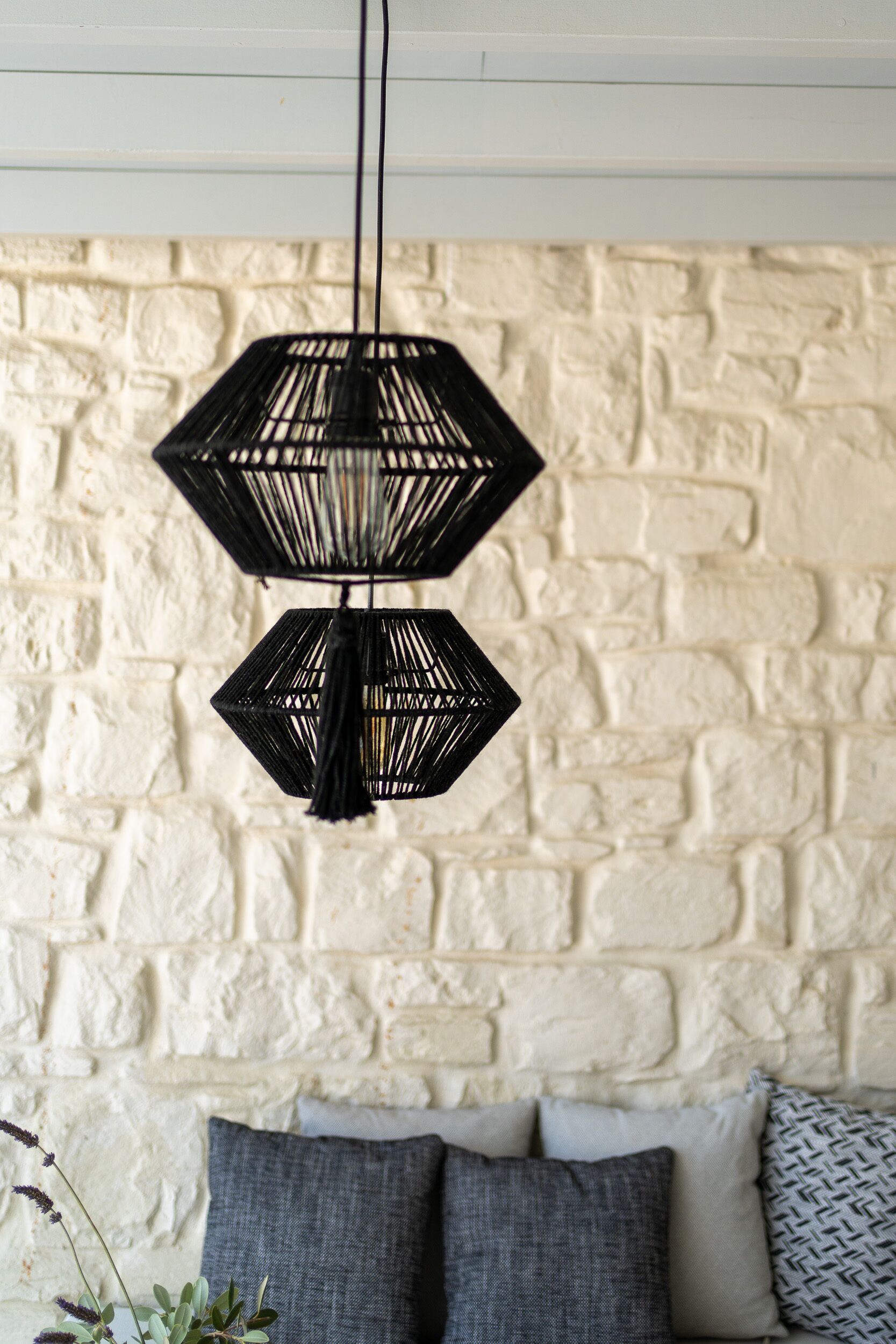 A room with a white brick wall, a black hanging light fixture, and a sofa with grey cushions.