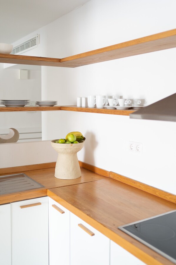 A kitchen with wooden countertops, white cabinets, a bowl of fruit, and a range hood.
