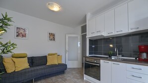 A modern kitchen with white cabinets, a built-in oven, and a red coffee maker. - Apartments Adela II (Novalja)