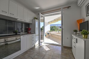 A modern kitchen with white cabinets, a built-in oven, and a sliding glass door leading to an outdoor patio with a table and chairs. - Apartments Adela II (Novalja)