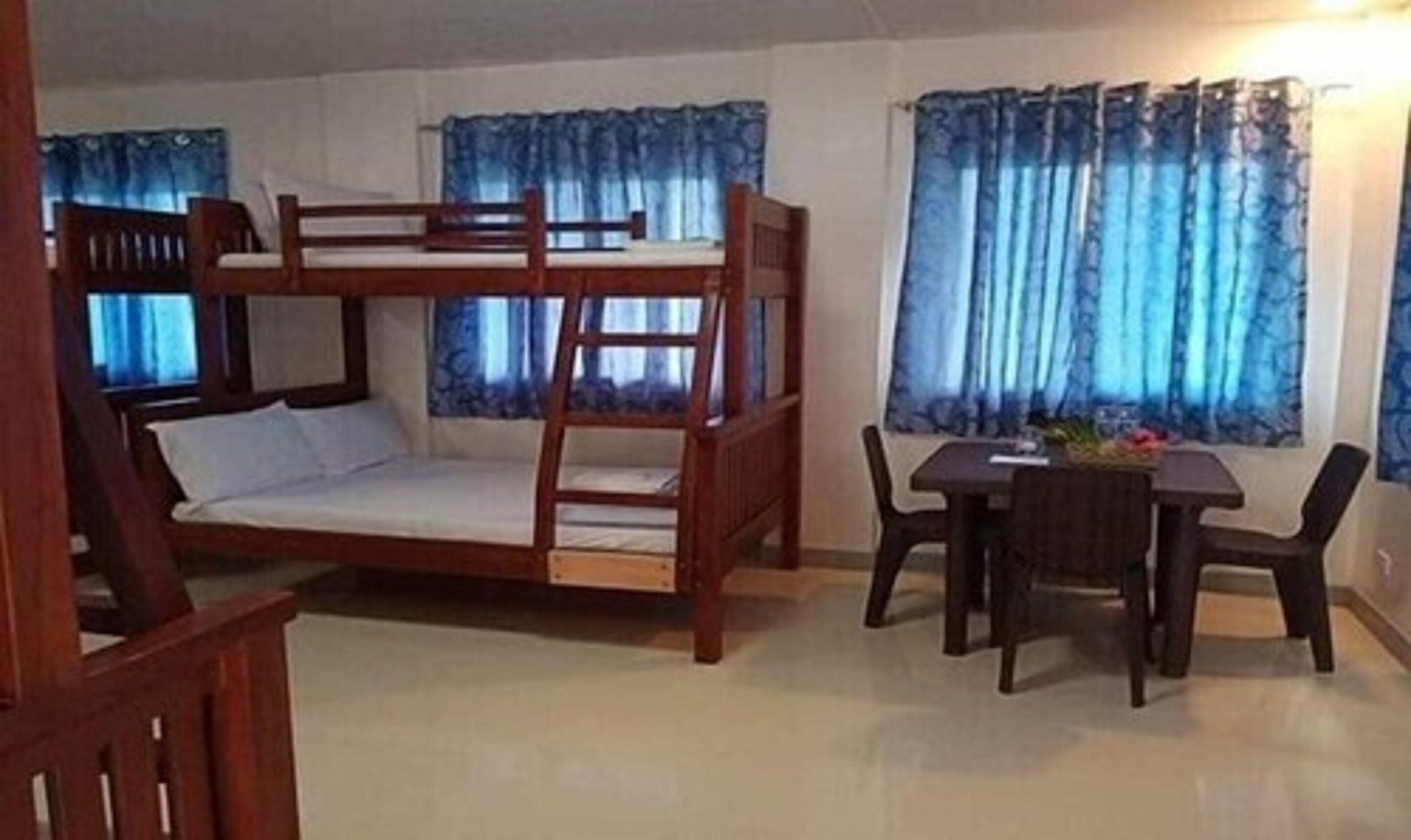 A bunk bed with a wooden frame and white bedding, a dining table with chairs, and blue curtains on the windows.