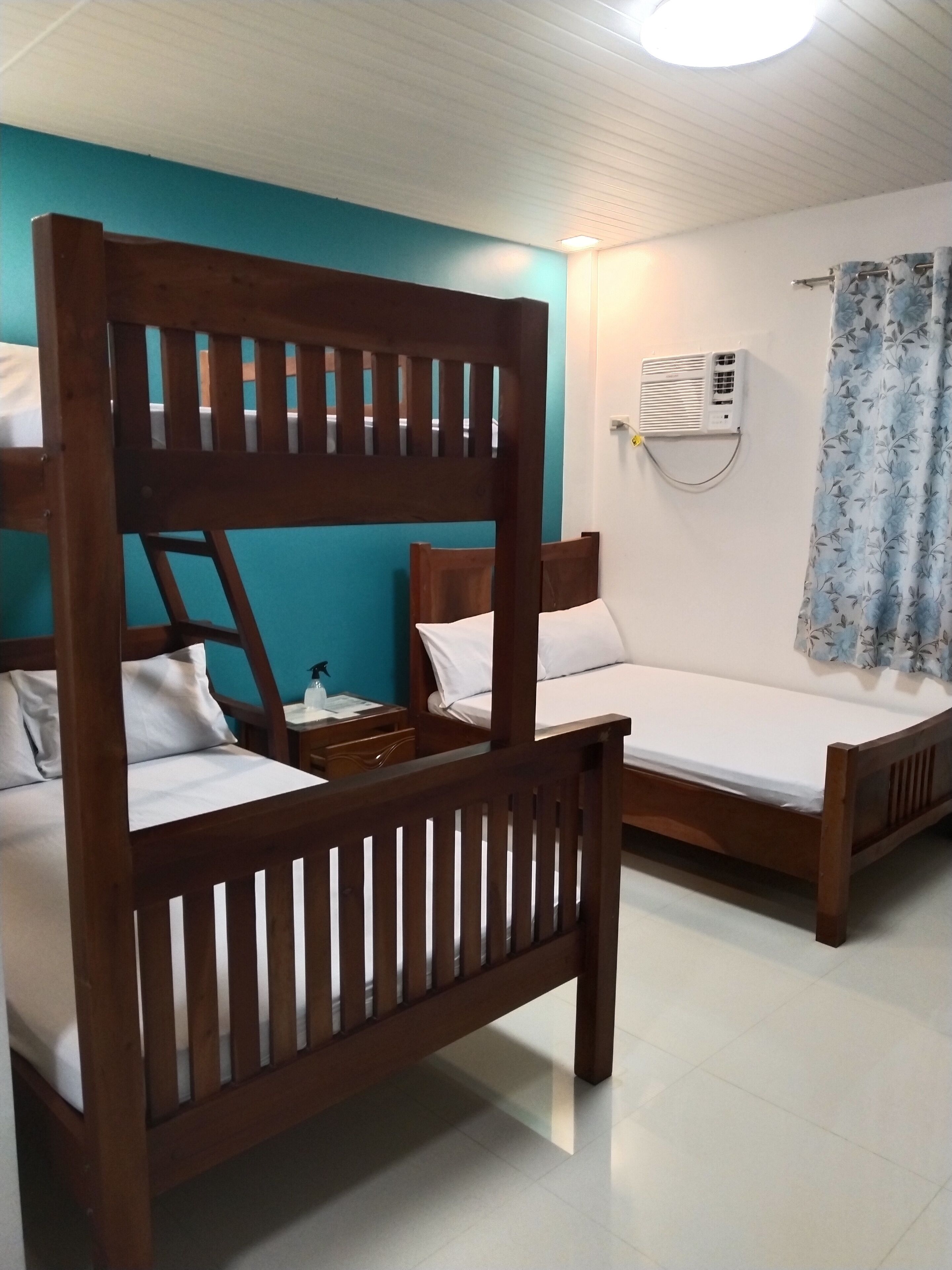 A room with two wooden bunk beds, a white air conditioning unit on the wall, and a blue curtain.