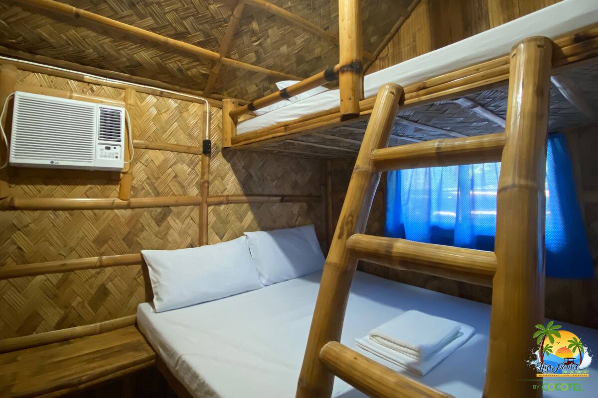 Ein Bettgestell aus Bambus mit einer weißen Matratze und Kissen, eine Klimaanlage an der Wand und ein Fenster mit blauen Vorhängen.