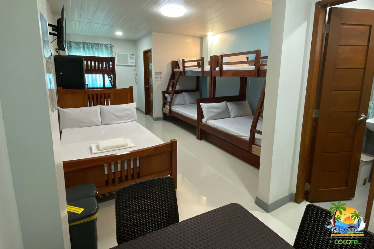 Ein Hotelzimmer mit Bett, Schreibtisch, Stuhl, Etagenbetten, Fernseher und einer Tür.