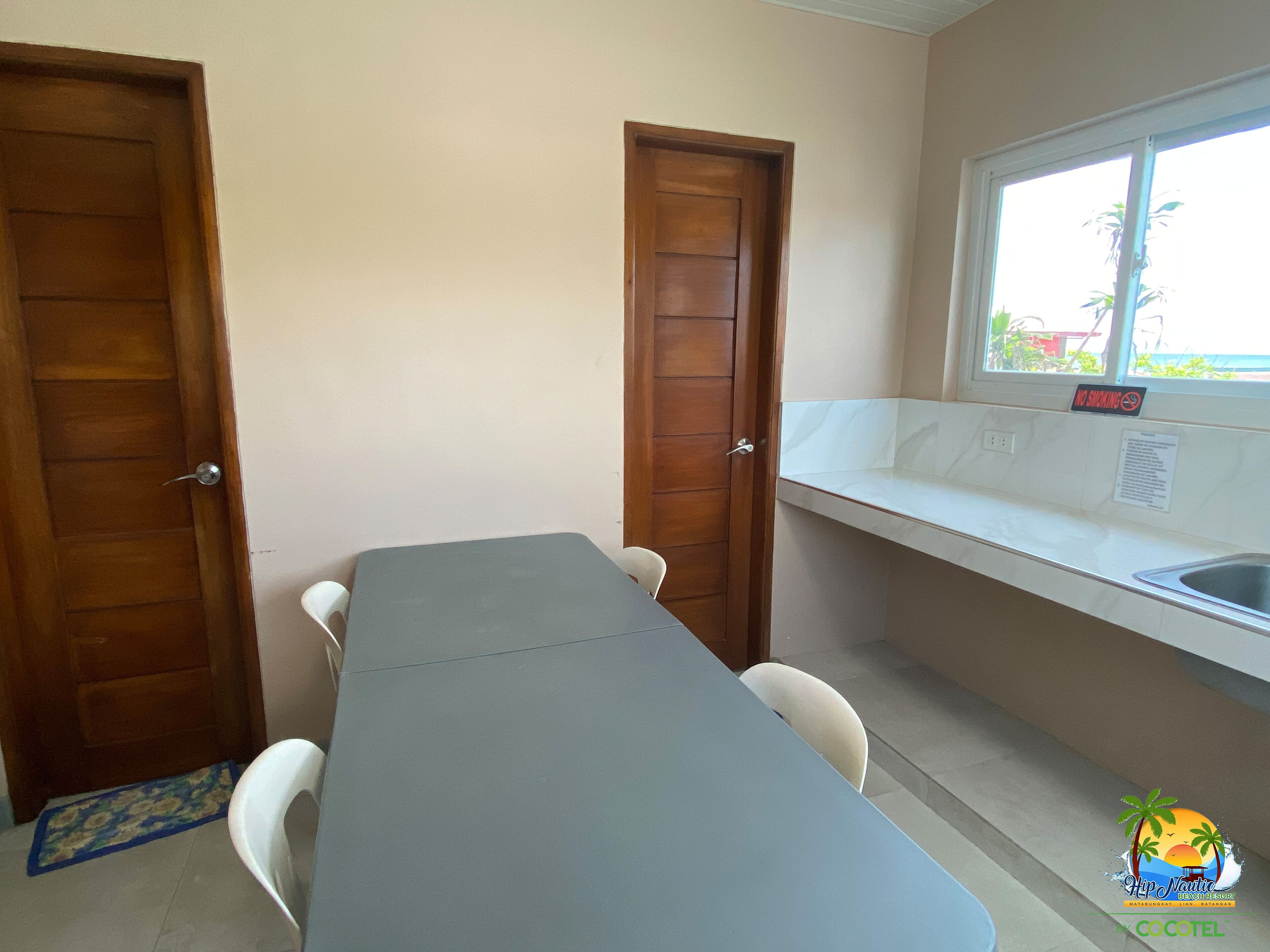 A small kitchenette with a table, two chairs, a window with a 'No Smoking' sign, and a tiled backsplash.