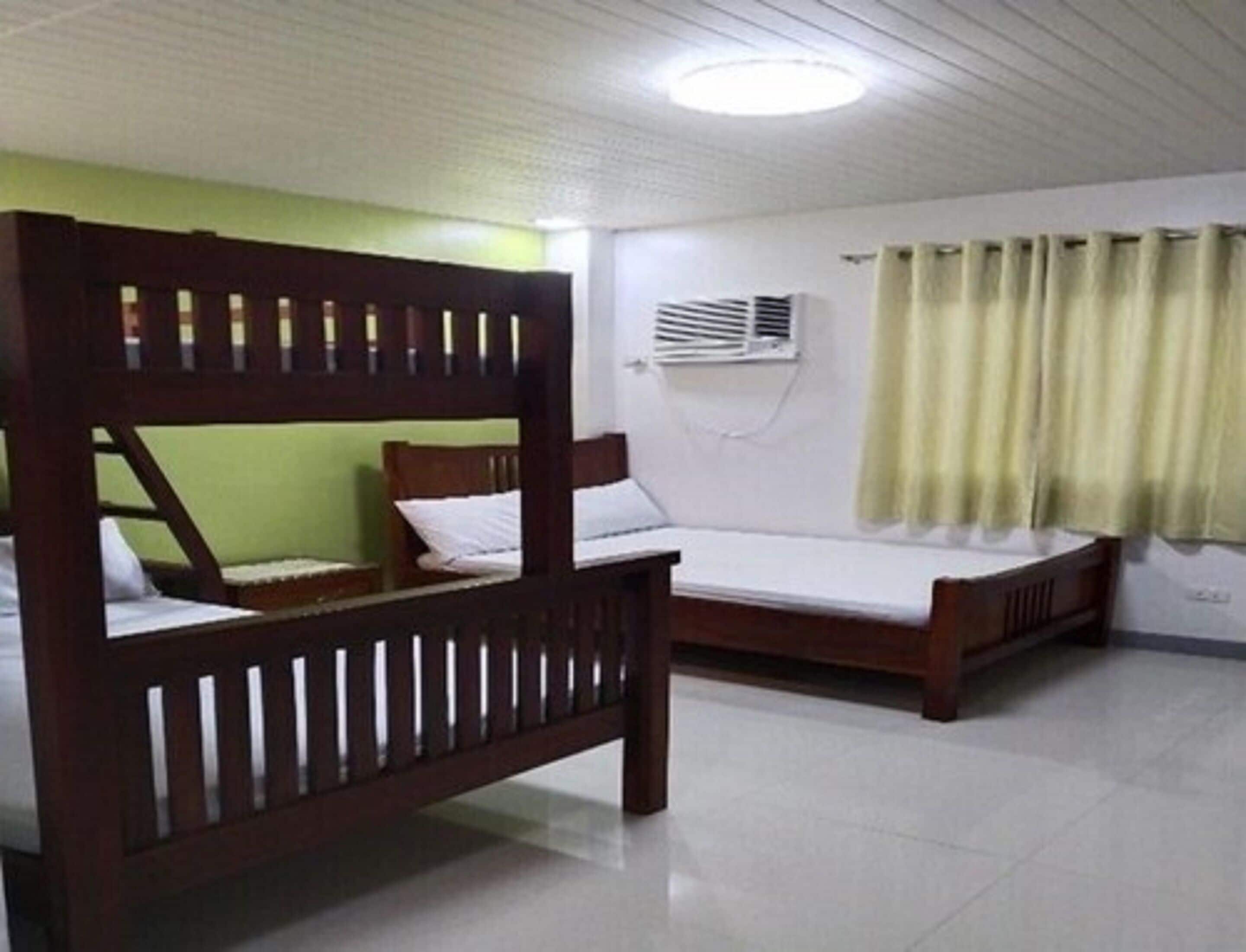 A room with two wooden bunk beds, a white air conditioning unit, and a window with curtains.