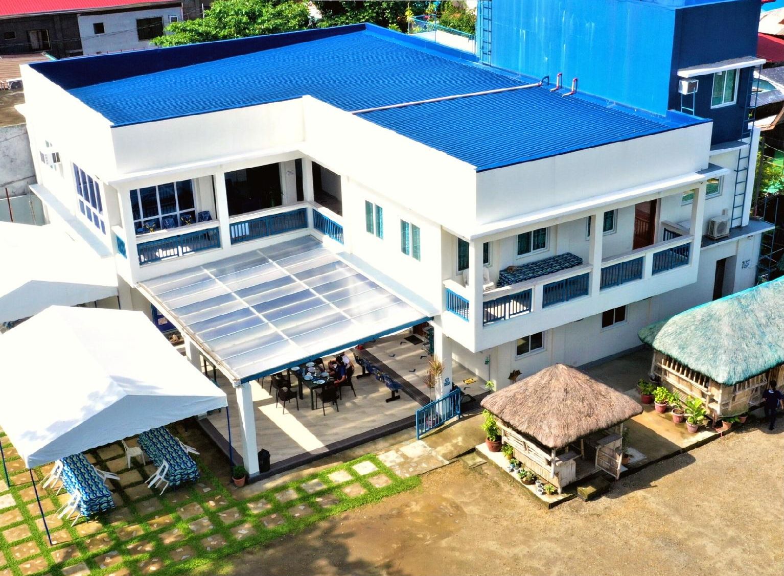 Un hotel moderno con techo azul, varios balcones y una zona de comedor exterior cubierta.