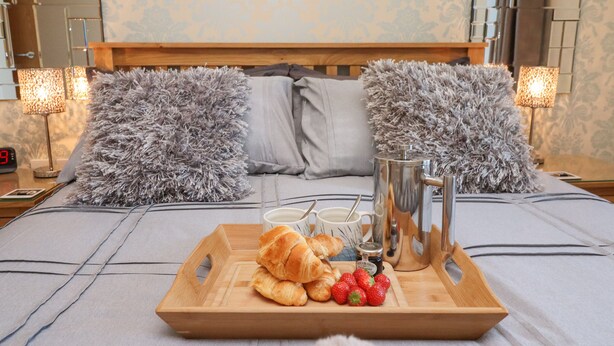 Ein ordentlich gedeckter Frühstückswagen auf einem Bett mit weichen Kissen, ein Nachttisch mit Lampe und ein Spiegel an der Wand.