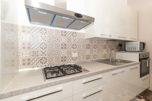 A modern kitchen with patterned tiles, a gas stove, a microwave, and stainless steel appliances. - Cozy and functional apartment perfect to accommodate 4 people and located in the heart of the Lingotto area, ideal for work, tourism and study. We are just a few minutes far from the hospital area (Molinette, San Lazzaro Dermatological Hospital, Regina M (Torino)