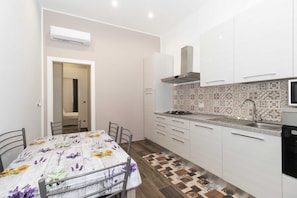 A kitchen with white cabinets, a patterned backsplash, and a dining table with a floral tablecloth.