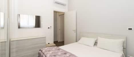 A bedroom with a bed, a dresser, a mirror, and an air conditioning unit.