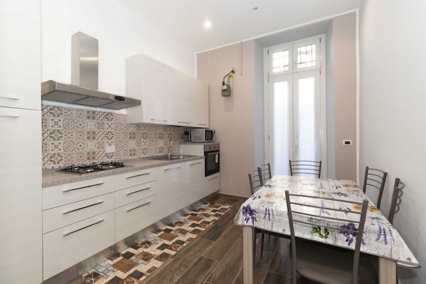 A compact kitchen with white cabinets, a gas stove, a microwave, and a patterned backsplash.