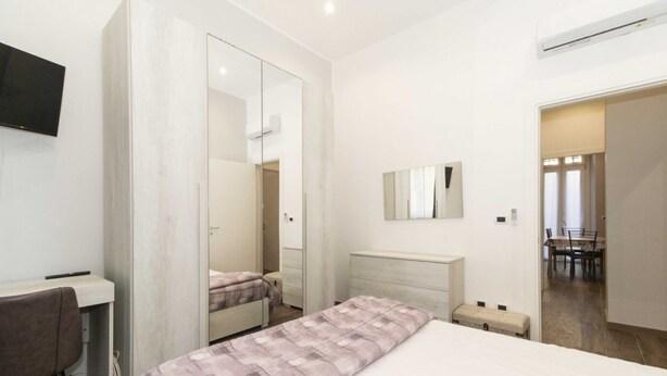 A modern hotel room with a bed, a desk, a chair, a mirror, and a television. - Cozy and functional apartment perfect to accommodate 4 people and located in the heart of the Lingotto area, ideal for work, tourism and study. We are just a few minutes far from the hospital area (Molinette, San Lazzaro Dermatological Hospital, Regina M (Torino)