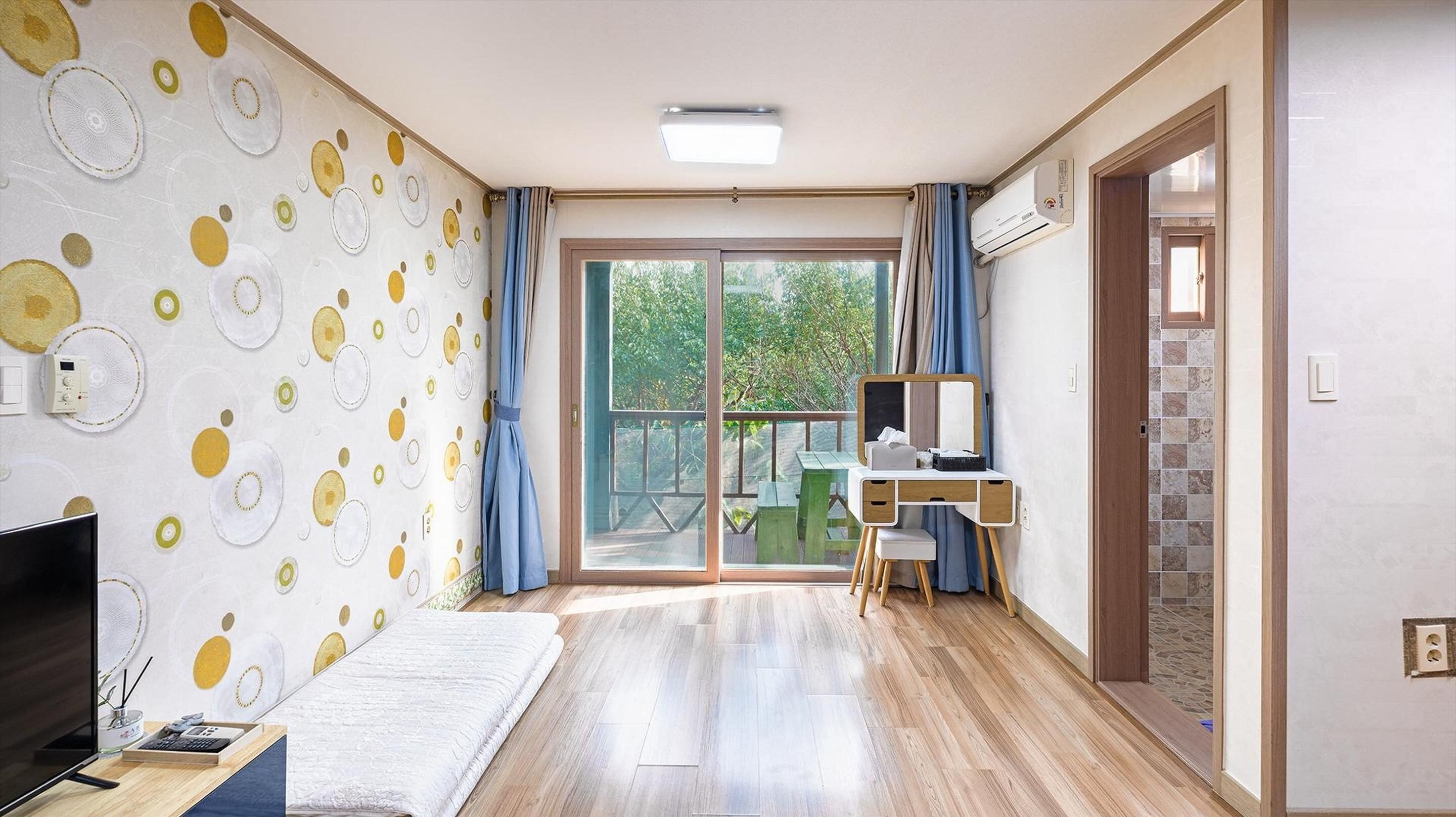 A modern room with a large window, a desk with a chair, a TV, and a patterned wall.