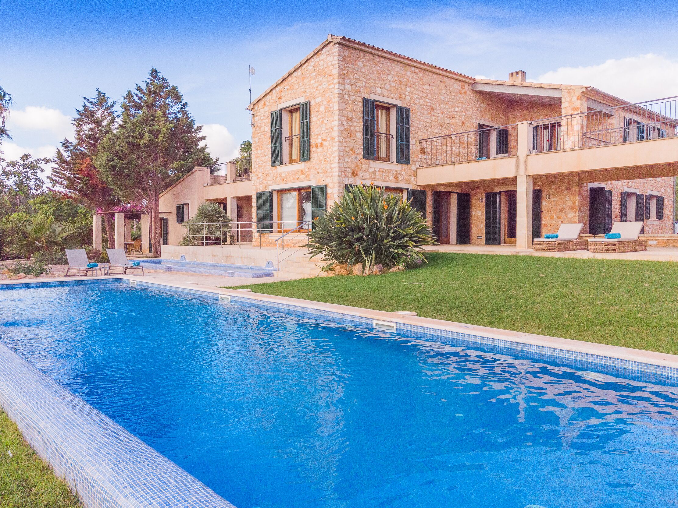 A two-story stone house with a swimming pool, outdoor seating, and a well-maintained lawn.