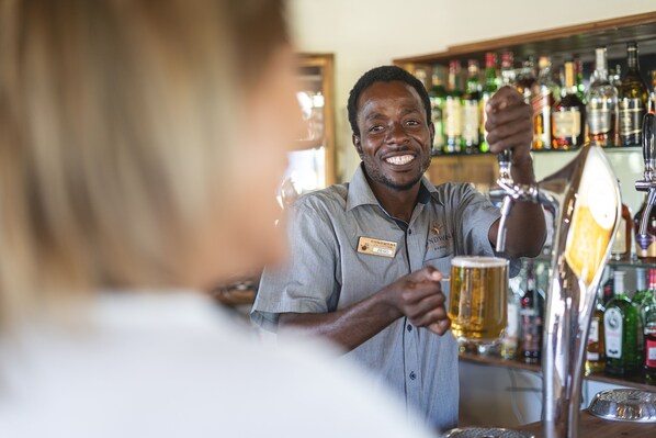 A bartender serving a beer at a bar with shelves of liquor bottles in the background.