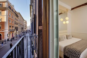 A hotel room with a bed, a view of a city street, and a balcony with railings. - Relais Luxury Corso (Rome)