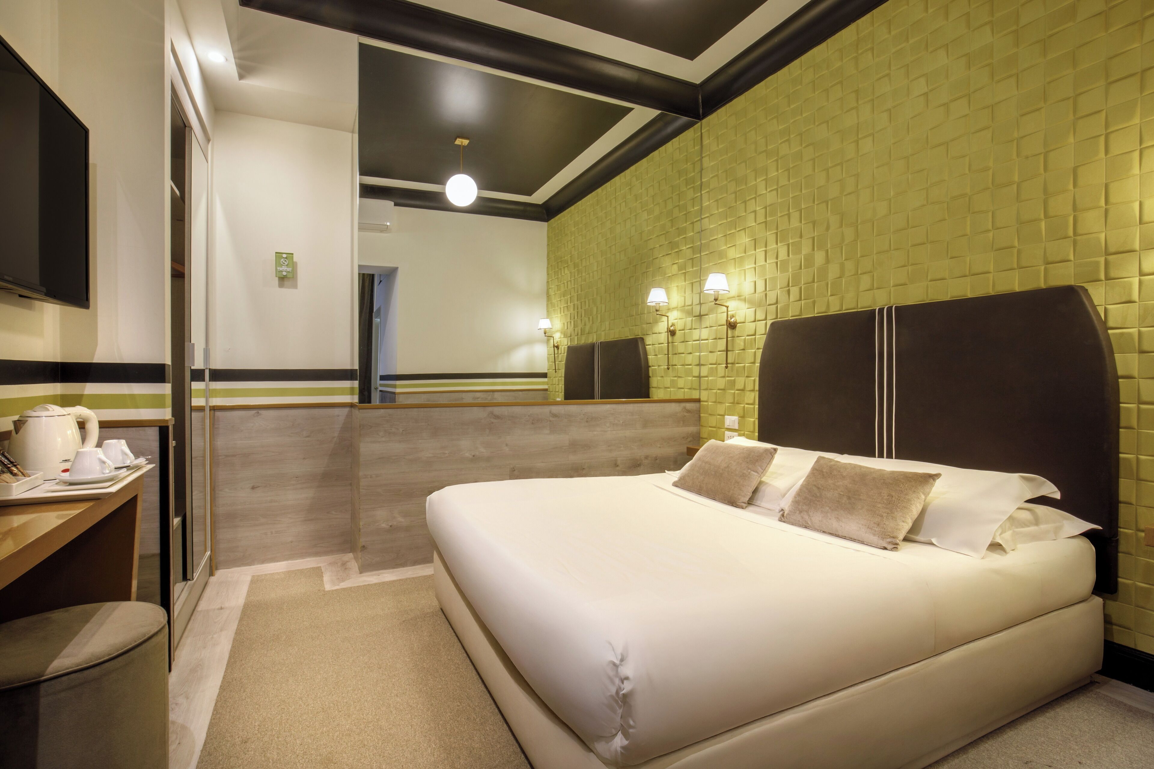 A hotel room with a bed, a desk, a chair, a mirror, and a wall with a textured pattern.
