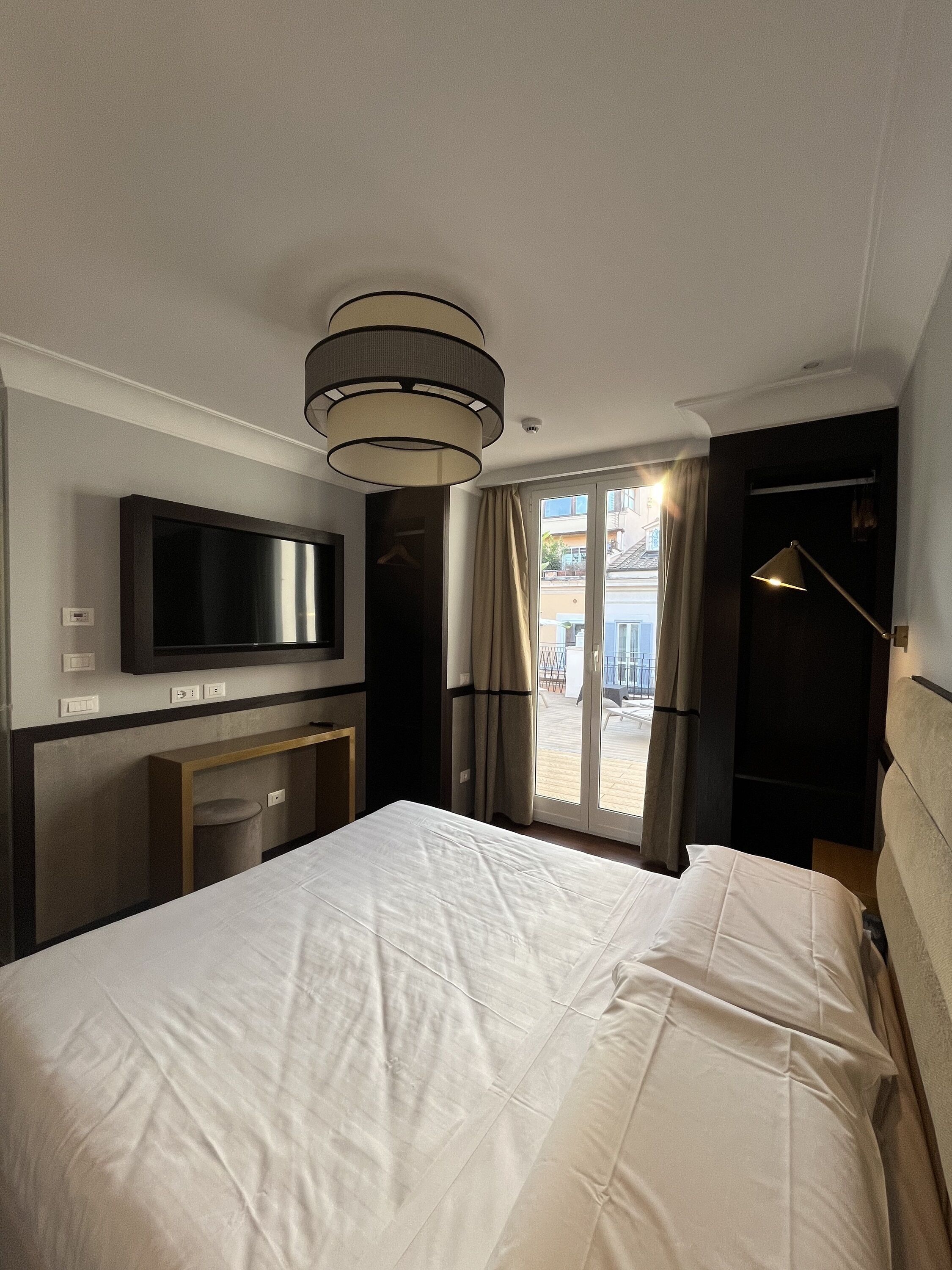 Una camera d'albergo con un letto grande, una TV montata a parete, una scrivania con una sedia e vista sul balcone esterno.