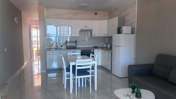 A modern kitchen with white cabinets, a dining table with chairs, a refrigerator, and a small round table with a plant. - Los Gigantes, Fantastic 1 Room, balcony (Acantilados de Los Gigantes)